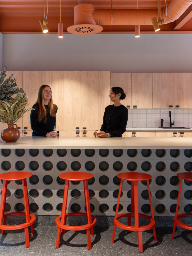 2 people chatting in the kitchen next to a concrete tiled counter with red stools